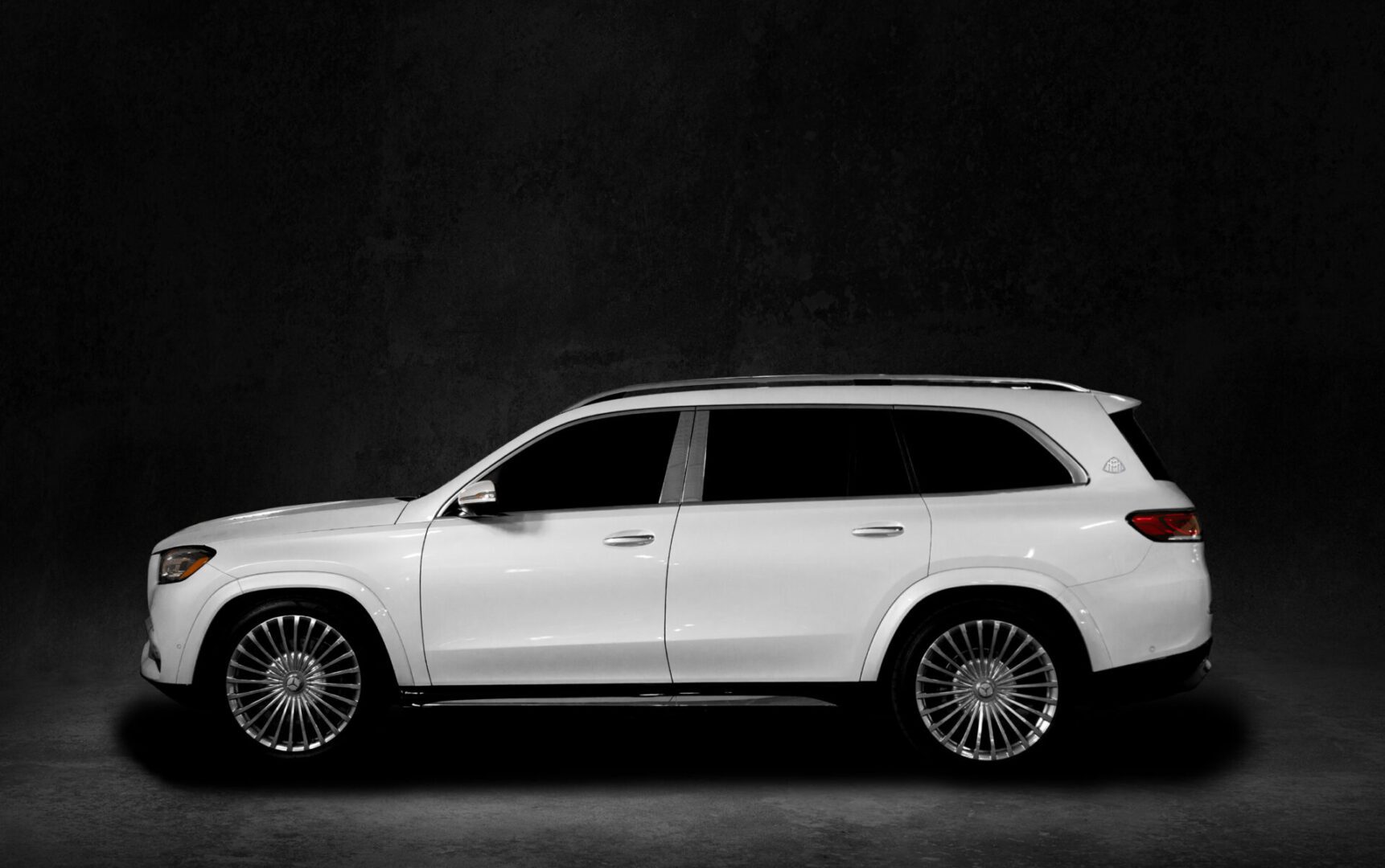 A white car is parked in front of a black wall.