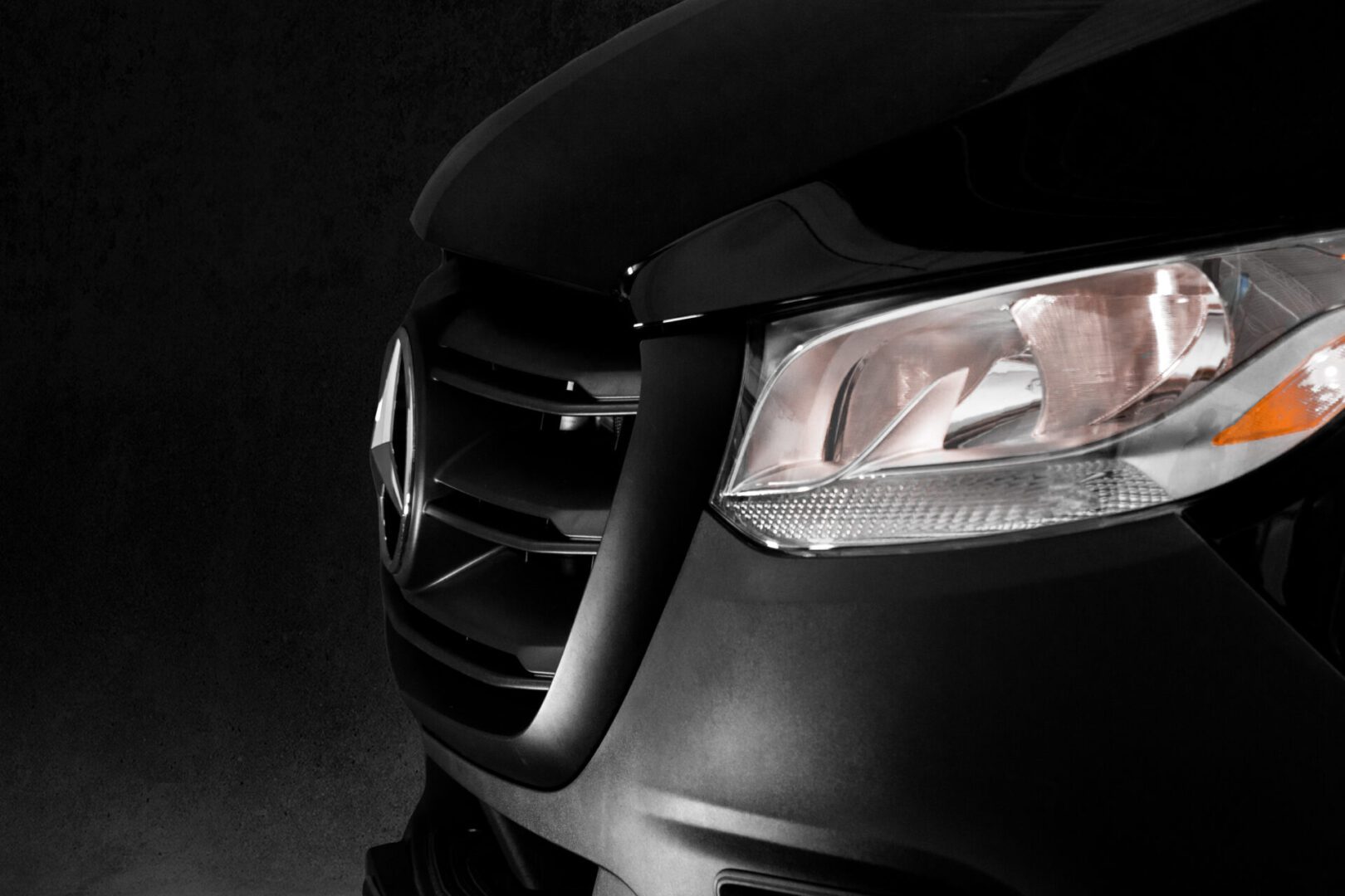 A close up of the front of a car with its headlights on.